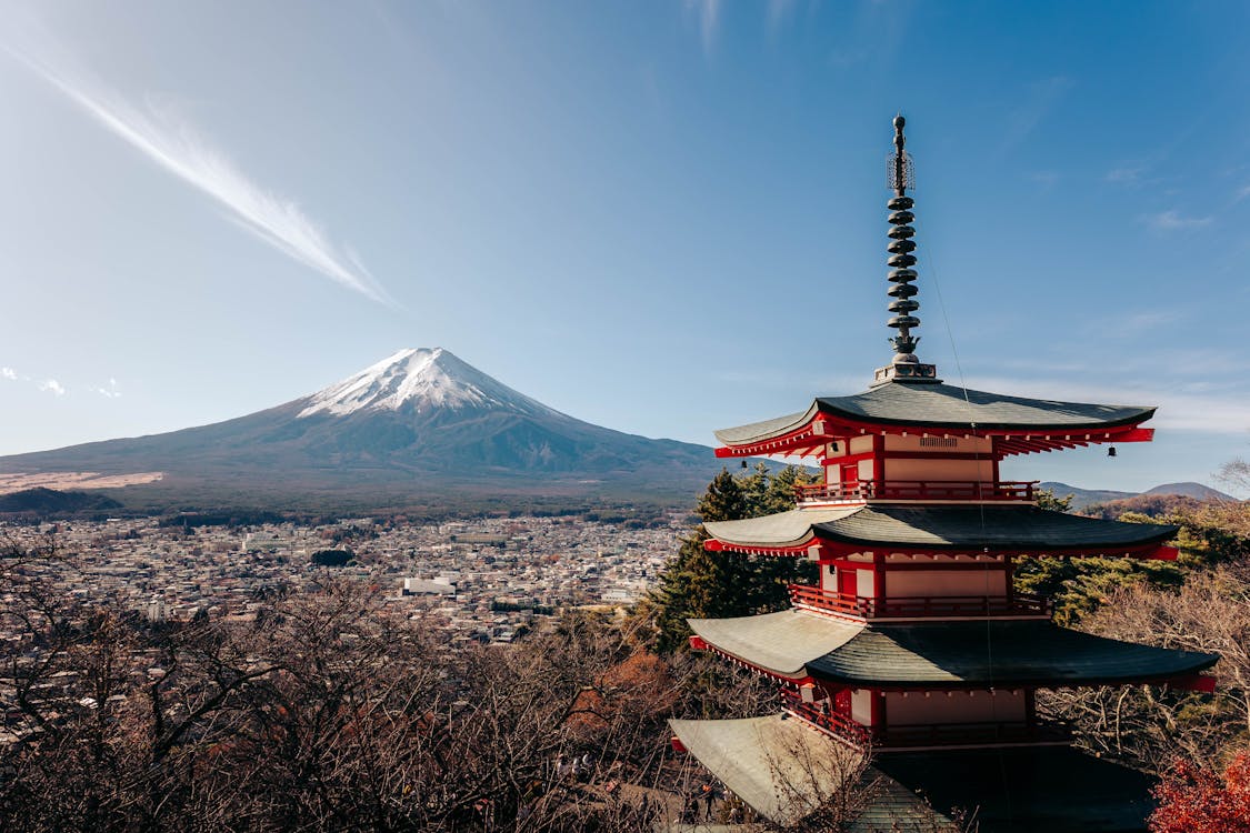Snow-capped Mount Fuji rising above a traditional red pagoda surrounded by Japanese pine trees